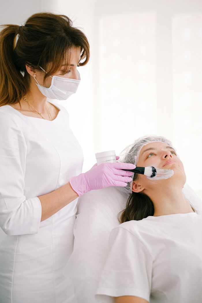 A beautician applies a facial mask to a customer in a bright spa room.